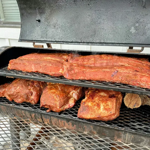 Offset smoker loaded with seasoned bacon slabs and pork butts